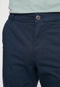 Navyblå bomullsmixade byxor med en slät textur, utrustade med knäppning framtill, diskreta sömdetaljer och sidofickor.