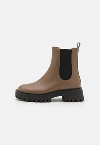 Bruine leren enkelboot met zwarte elastische zijkanten, ronde neus en chunky zwarte rubberen zool met gestructureerd profiel.