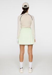 Maglia a maniche lunghe beige chiaro con dettagli neri, abbinata a una gonna plissettata verde menta. Calze bianche fino al ginocchio e sneakers beige completano il look.