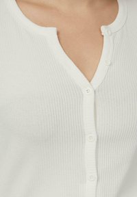 Biały prążkowany top na guziki z dekoltem w serek, wyposażony w trzy okrągłe białe guziki i miękką teksturę.