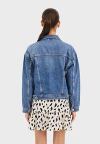 Spijkerjasje, lichtblauw, vervaagde wassing, losse pasvorm met lange mouwen, knoopmanchetten en zichtbare stiksels. Gecombineerd met een gerimpelde zwart-witte rok.