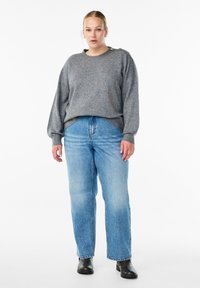 Pull en tricot gris avec un col rond et des accents de boutons sur une épaule, associé à un jean droit bleu clair et des bottines noires.