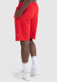 Rode sportieve shorts van zacht materiaal, met een elastische tailleband, zijzakken en een klein logolabel op de zoom. Gecombineerd met witte sokken.