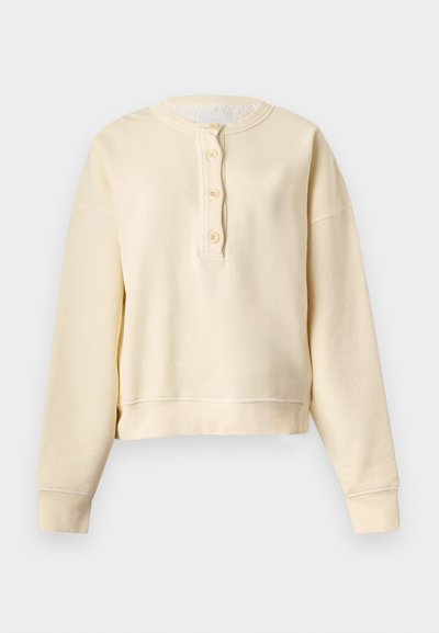 Μπλούζα Henley με μακριά μανίκια σε κρεμ απόχρωση, ριμπ μανσέτες, στρογγυλή λαιμόκοψη και πατιλέτα με τέσσερα κουμπιά μπροστά.