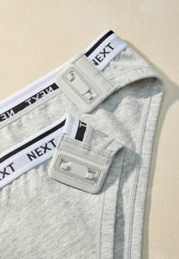 Grey cotton underwear with a white waistband featuring black lettering. Includes adjustable straps with rectangular plastic hardware.