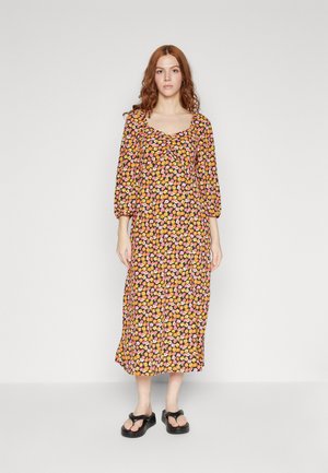 Robe noire fleurie avec un décolleté carré, des manches trois-quarts et une coupe fluide, ornée de fleurs orange et roses. Tongs noires.