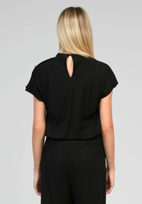 Haut noir avec des manches courtes, une ouverture en forme de clé à l'arrière et des détails subtils aux épaules. Texture lisse et coupe décontractée.