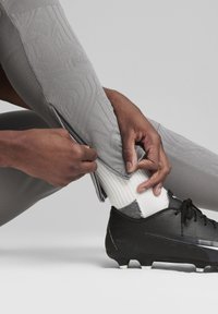 Grijze sportleggings met textuurpatronen, een rits bij de enkel, gecombineerd met een zwarte voetbalschoen en een witte sok.