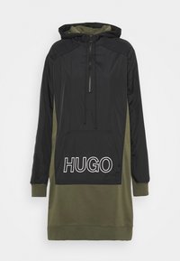 Sweat à capuche avec un haut noir et un bas vert olive, doté d'une poche avant et d'un grand logo blanc "HUGO" sur le côté gauche.
