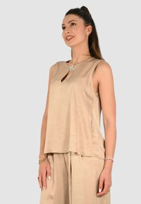 Top beige senza maniche con scollo a goccia, realizzato in tessuto texturizzato, caratterizzato da una vestibilità ampia che cade dolcemente sul corpo.