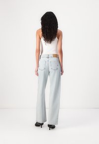 Svetlo modri široki jeans z srednjim pasom, z rjavim usnjenim zilicami na hrbtni strani in dvema zadnjima žepoma. Gladka denim tekstura.