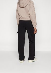 Ljusbeige croppad hoodie med huva och logodetalj på sidan, i kombination med svarta cargobyxor med fickor och rak skärning. Vita sneakers.