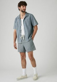 Camicia a righe a maniche corte in azzurro chiaro e bianco, abbinata a pantaloni corti coordinati. Presenta chiusura a bottoni e vita con cordoncino. Design casual.