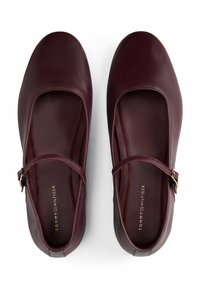 Ballerines en cuir bourgogne avec un bout arrondi, une sangle réglable et un biais doré. Texture lisse avec un minimum de détails de couture.