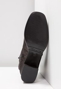 Semelle noire d'une botte à bout carré avec grip texturé, talon bloc, et le nom de la marque "Tamaris" embossé près de la voûte plantaire.