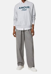 Grijze sweatshirt met "AMOUR Paris" opdruk, gelaagd over een wit shirt, gecombineerd met grijs gestreepte wijde broek en witte sneakers.