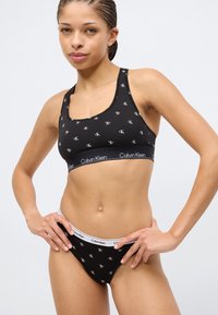 Μαύρο βαμβακερό αθλητικό σουτιέν και αντίστοιχο σλιπ με επαναλαμβανόμενο μοτίβο λογότυπου και αντίθετη μέση με το κείμενο "Calvin Klein".