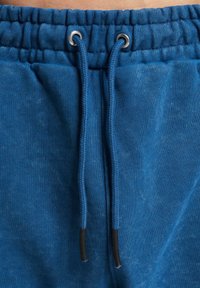 Blue cotton joggers with a drawstring waist, featuring silver grommets and textured fabric. Soft and casual design, suitable for relaxed wear.