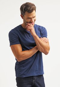 Navy blue, crew-neck t-shirt made of soft material, fitted design showcasing short sleeves, worn with dark jeans, arms crossed.