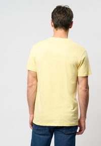 Tricou galben cu mânecă scurtă și guler rotund, fabricat dintr-un material moale, având o textură netedă, asortat cu blugi din denim albastru.