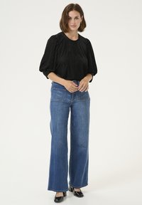 Blusa nera a righe verticali con maniche a palloncino, abbinata a jeans in denim blu a gamba larga. L'outfit presenta un design pulito e un contrasto di colori classico.