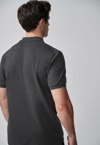Polo de color gris oscuro con cuello y mangas cortas, confeccionado en una tela suave. Presenta un diseño liso sin patrones ni acentos visibles.