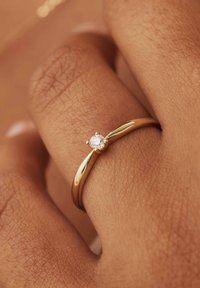  gouden ring met een gladde, gepolijste band en een enkele, ronde diamant in het midden. Draag op een hand met een gestructureerde huid.