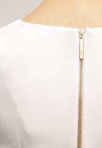 Tissu de robe blanche avec une texture lisse, comprenant une fermeture éclair dorée à l'arrière, ajoutant un détail accent subtil.
