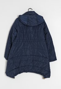 Navy puffer jacket, hooded, features quilted texture, wide shape, and drawstring hem. Lightweight material hangs on a hook.