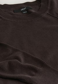 Ciemnobrązowy sweter z okrągłym dekoltem wykonany z miękkiego materiału. Posiada ribbowany dekolt i mankiety, widoczne szwy oraz metkę z napisem "NEXT."