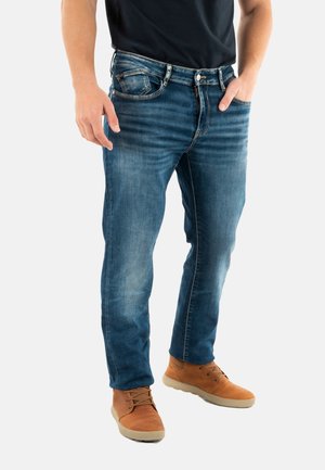 Vaqueros de denim en azul medio con un ligero desgaste, diseño de cinco bolsillos y corte recto, combinados con zapatos marrones.