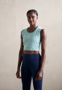 Svijetloplava crop majica s okruglim izrezom, bez rukava, s Nike logom; uparena s tamnoplave tajice visokog struka. Glatka tekstura.
