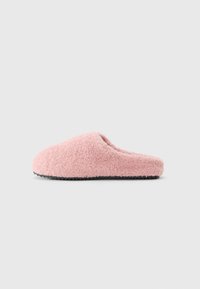 Myk rosa fleece tøfler med svart teksturert såle, sett fra siden på lys grå bakgrunn.