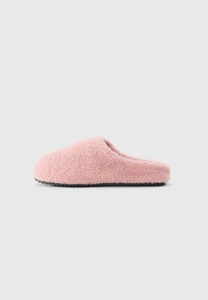 Myk rosa fleece tøfler med svart teksturert såle, sett fra siden på lys grå bakgrunn.