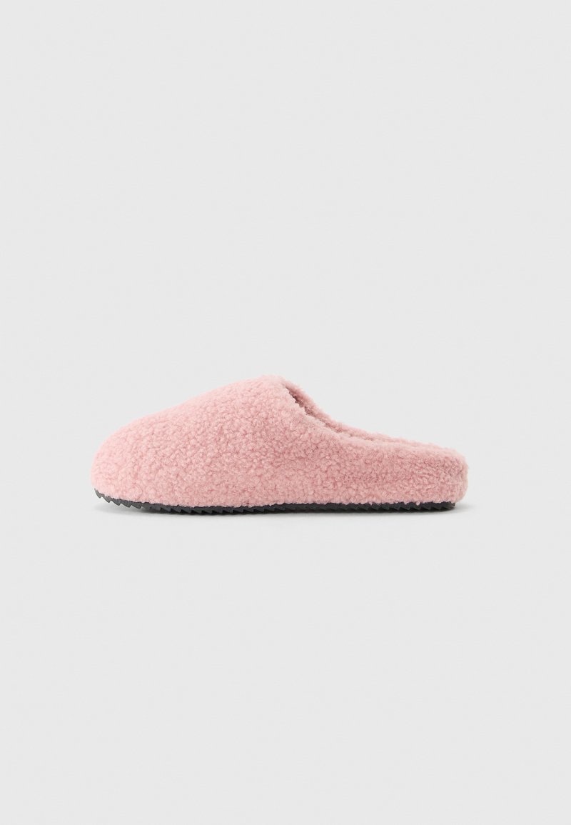 Myk rosa fleece tøfler med svart teksturert såle, sett fra siden på lys grå bakgrunn.