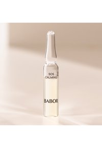 Tydlig glasampull fylld med ljusgul vätska, märkt "SOS CALMING" och "BABOR" i svart text, med en avsmalnande hals.