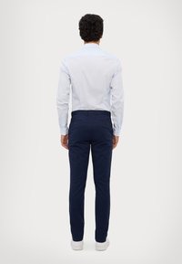 Lys blå langermet skjorte med knappede mansjetter, kombinert med marineblå slim-fit chinos. Hvite sneakers synlige nederst. Minimalistisk design.