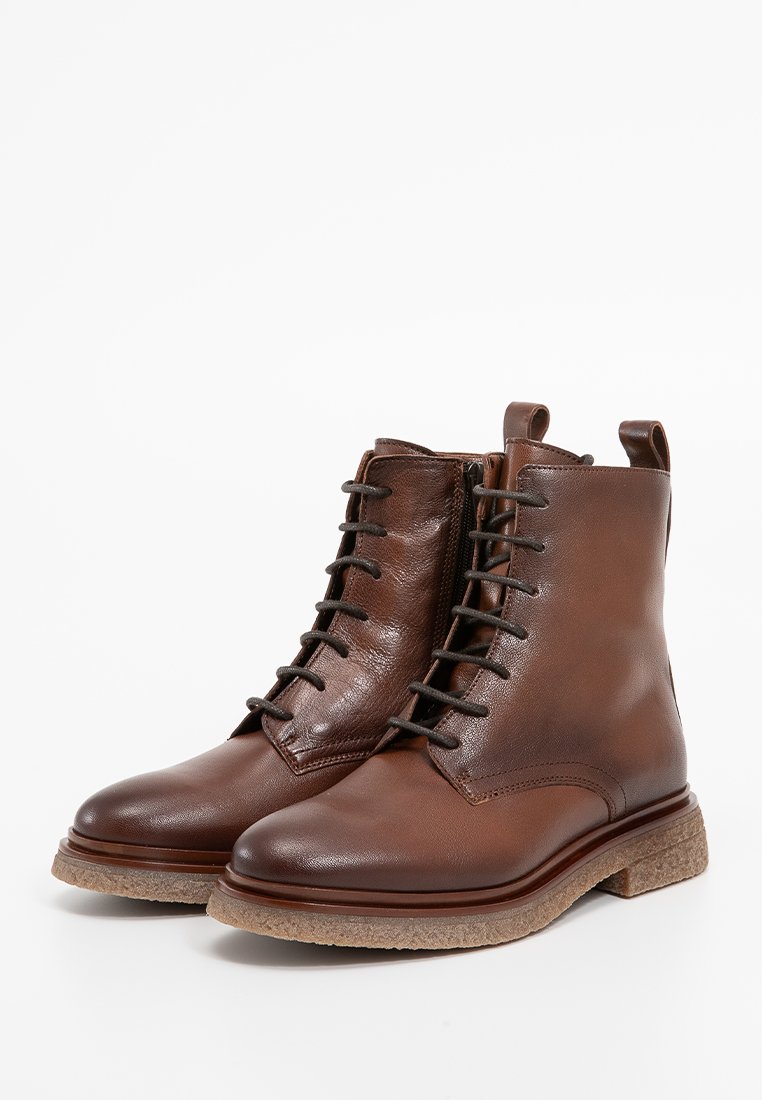Braune Leder-Stiefeletten mit glatter Oberfläche, Schnürdesign und seitlichem Reißverschluss. Auffällige strukturierte Sohle in hellbrauner Farbe.