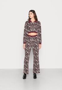 Conjunto de duas peças com padrão de zebra em creme e bordô, apresentando uma blusa cropped com botões e calças largas, feitas de um tecido de malha texturizada.