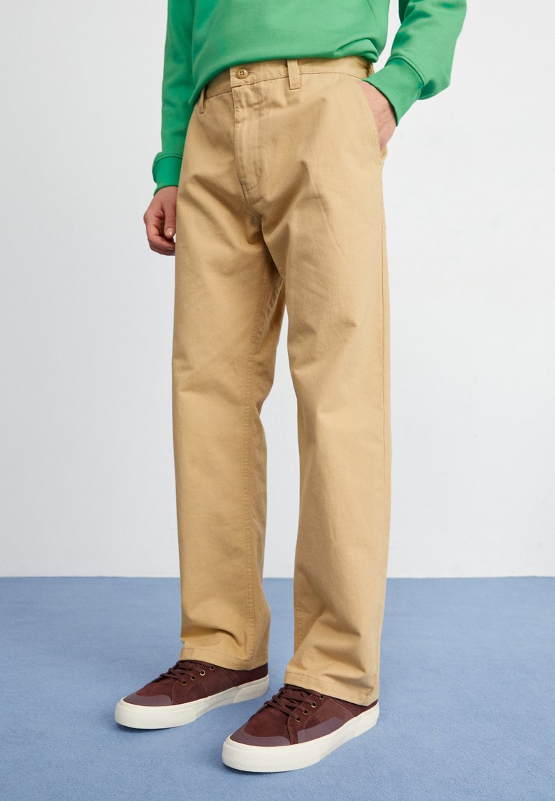 Beige bomullsbusker med en avslappet passform, med knappåpning og sidelommer, paret med mørk burgunder sneakers.