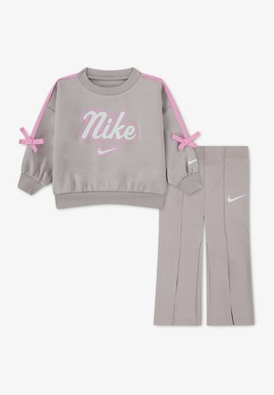 Sweat-shirt Nike gris clair avec des bandes roses sur les épaules et des nœuds, assorti à des leggings gris clair avec des logos Nike blancs.
