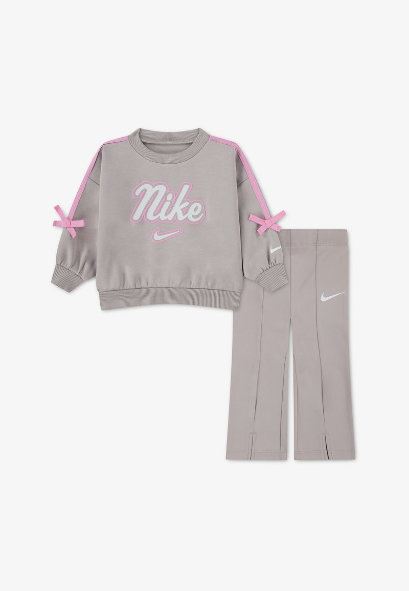 Φωτεινό γκρι φούτερ Nike με ροζ ρίγες στους ώμους και φιόγκους, σε συνδυασμό με αντίστοιχο φωτεινό γκρι κολάν με λευκά λογότυπα Nike.