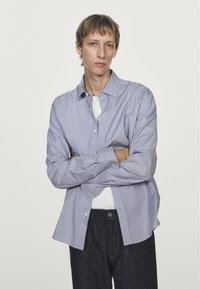 Striped button-up shirt in blue and white, long sleeves, relaxed fit, paired with dark denim jeans. Smooth fabric with classic collar.