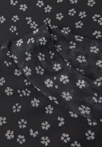Sort meshstof med et spredt hvidt blomstermønster. Teksturen er åndbar med en let glans i lyset.