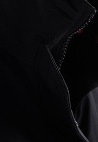 Sort jakke med lynlås foran, glat tekstur og en afslappet pasform. Detaljer omfatter en struktureret lynlås og skjulte lommer.