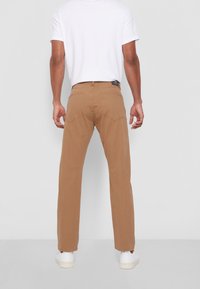 Braune Chinos aus Baumwolle mit geradem Bein, ausgestattet mit Gesäßtaschen und einem lockeren Schnitt. Kombiniert mit weißen Sneakern.