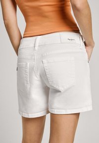 Valkoiset denim-shortsit, joissa on istuva malli, kaksi takataskua, suora helma ja merkkilogo vyötärönauhassa.