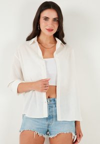 White sheer button-up shirt with rolled sleeves, paired with light blue denim shorts. The fabric appears lightweight and slightly textured.