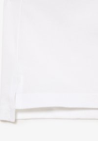Weißer Baumwollstoff mit strukturierter Oberfläche, ausgestattet mit einem sauberen Saum und seitlichen Schlitzdetails, die für Atmungsaktivität und Komfort sorgen.