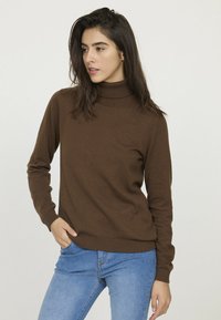 Pull à col roulé marron, côtelé, en tissu doux, avec des manches longues et une coupe ajustée, associé à un jean bleu clair.